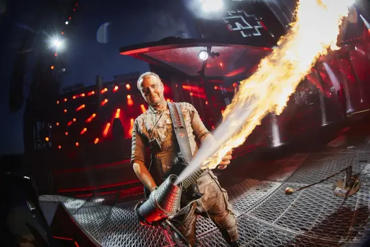 Till Lindemann z Rammstein z miotaczem ognia na scenie. Koncert trwa, a fani zastanawiają się, ile trwa koncert Rammstein.