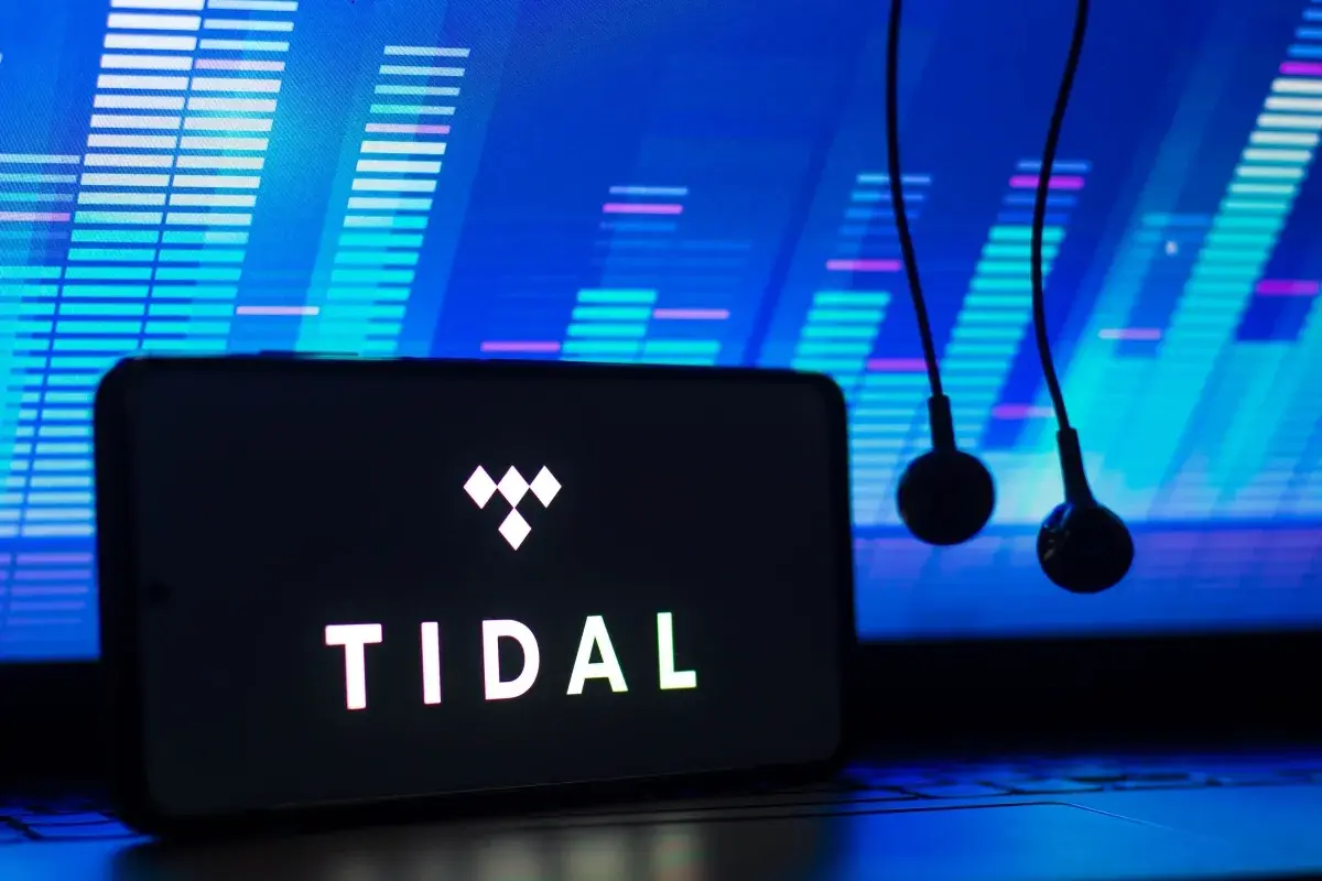 Smartfon z logo TIDAL i słuchawkami na tle wykresu dźwiękowego.
