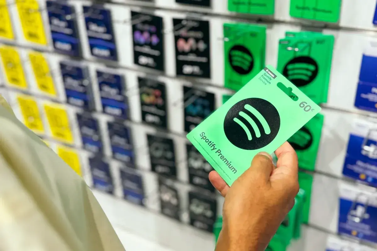 Ręka trzyma zieloną kartę podarunkową Spotify Premium z ceną 60€. W tle widać rząd innych kart.
